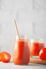Fototapeta na wymiar Glass of tomato juice with vegetables on white brick wall background