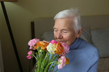 Portrait of happy elderly woman receiving a bouquet of colorful ranunculus flowers and inhaling the sweet aroma. Senior lady sniffing buttercups. Close up, copy space, background.