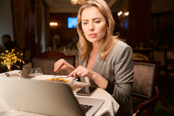 Businesswoman reading work plan on laptop having dinner at restaurant