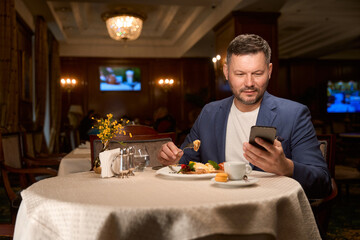 Businessman eating lunch and reading message on smartphone