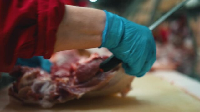 Meat processing factory, food production facility. Plant employee is cutting off carcasses