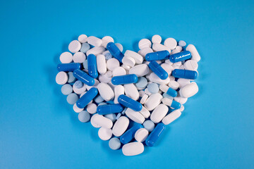 White pills and blue capsules in the shape of a heart on a blue background. Pills for heart health.