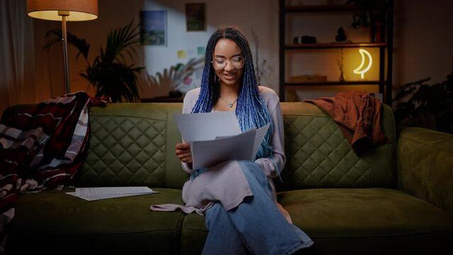 Contented young woman expressing positive emotions, reading essay article at home in the night time