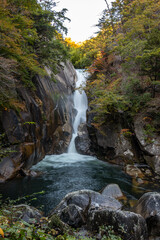 Fototapeta premium Senga Waterfall ( Sengataki ), A waterfall in Mitake Shosenkyo Gorge. Autumn foliage scenery view in sunny day. A popular tourist attractions in Kofu, Yamanashi Prefecture, Japan