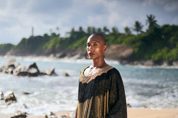 Flamboyant gay black male in luxury gown poses on scenic ocean beach. Trans sexual ethnic fashion...