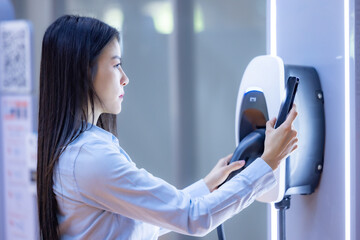 Young Asian woman holding the CCS 2 EV charging connector at EV charging station in department...