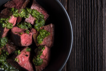 Fried slices of beef tenderloin in pesto sauce in a deep plate on a wooden table. Close - up.