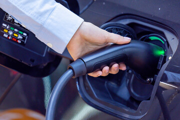 Woman holding the CCS 2 EV charging connector at EV charging station in department store. EV-electric vehicle charging connector for a vehicle. EV charging an electric car. Nature energy,Clean energy.