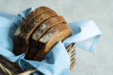 High angle of stack of rye bread slices in wicker basket with cloth napkin against blurred light background