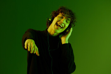 Man wearing headphones listening to music, dancing and singing with his eyes closed, DJ happiness and smile, hipster lifestyle, portrait green background mixed neon light, copy space