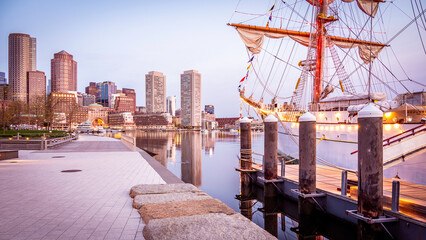 Fototapeta na wymiar View of Boston in Massachusetts, USA at The fan Pier and Boston Harbor at sunrise showcasing the skyline of the city and a vintage sailing boat anchored on the side.