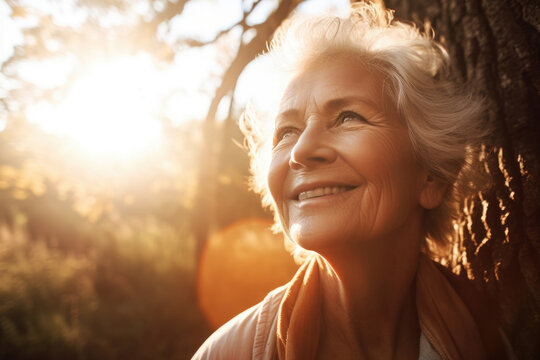 Generative AI image of portrait of smiling aged female with gray hair and wrinkles standing and looking away while admiring green forest against blurred trees in sunlight