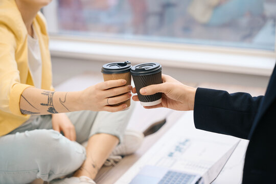 Friendly colleagues clinking paper glasses with coffee to-go