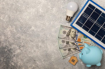 Flat lay composition with solar panel, led lamp. house model and piggy bank on a marble background. The concept of saving money and clean energy. The concept of ecology and sustainable development.