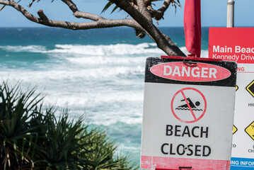 A sign shows beach closed and a red flag in front an agitated ocean
