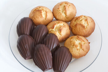 Homemade muffins and Madeleine cookies in chocolate. They lie on a plate.