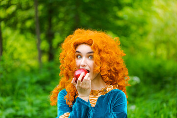 Curly red-haired girl fairy in nature with long curly hair in a blue dress eats