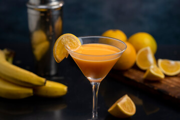 cocktail glass with orange juice shaker and natural oranges and bananas and splash with liquid flying in the air - obrazy, fototapety, plakaty