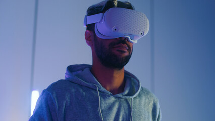 Young Middle East man putting on Virtual Reality headset for first time exploring VR world express amazed, surprised feeling of strange future atmosphere sit in RGB neon light gaming room