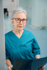 Gray-haired female medic stands in hospital corridor with MRI scan