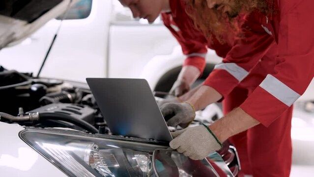 Close-up hand male mechanic Caucasian, opened hood car in order repair front car, two people helped repair find wrong spot car, there was laptop computer in front find way repair damaged spots.