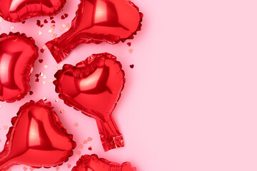 Red inflatable foil balloons in a heart shape and confetti. Compisition on a pink background with copy space.