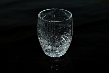 A glass made of crystal glass stands on a dark table surface.