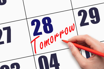 28th day of the month. Hand writing text TOMORROW on calendar date.