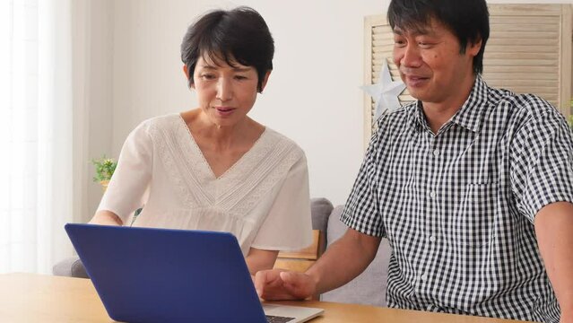 リビングでノートパソコンを見る熟年夫婦