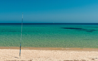 Fishing rod on a beach of golden sand, blue sky and turquoise sea. Leisure destination on the Mediterranean in Sardinia, Italy