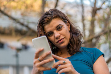 A beautiful latin woman using her smartphone outdoors looking at camera