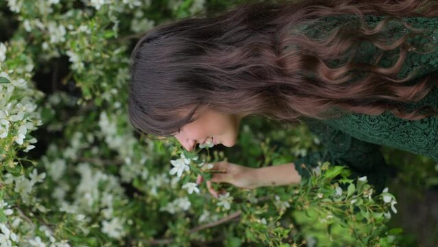 A young brunette in a hat fooling around and enjoying nature in front of a blooming apple tree. Holidaying out of town in blooming orchards. The concept of the spring season