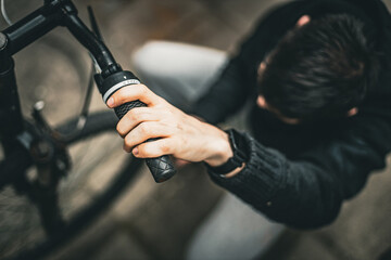 A young man holds the handlebars of a bicycle with his hand.