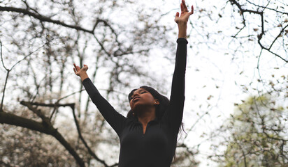 Happy and relaxed African woman raised her hands in the park, oneness with nature.
