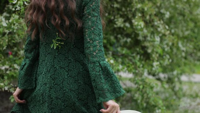 A young girl in a green dress walks with her back to a blooming apple tree in the city.