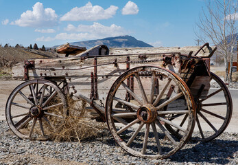 Fototapeta na wymiar Worn weathered buckboard wood wagon with mountains and blue sky background. Wood wheels are prominent.