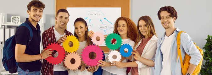 Team of male and female students work on project together. Group portrait of happy young people looking at camera, joining colorful gears and smiling. Education, integration, teamwork, success concept