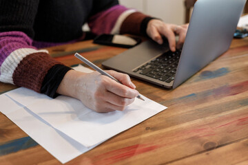 Business woman hands with pen writing notes on paper and working with the laptop