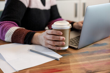 Woman's hand is working on a laptop and  a cup of coffee in the table
