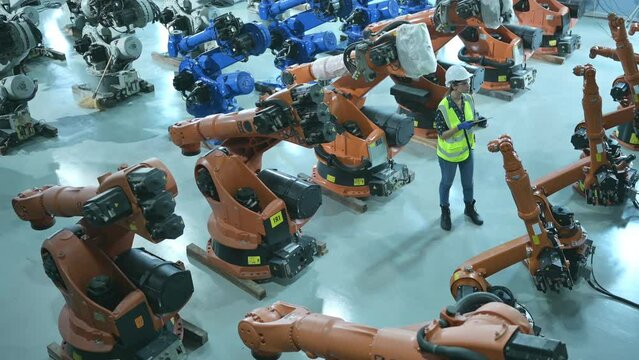 A female engineer installs a program on a robotics arm in a robot warehouse. And test the operation before sending the machine to the customer.