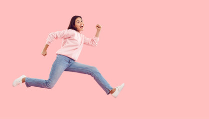 Fototapeta na wymiar Seasonal discounts. Funny energetic young woman rushes to shopping center in hurry for crazy discounts on sales. Woman in casual clothes running isolated on pink background. Web banner. Copy space.