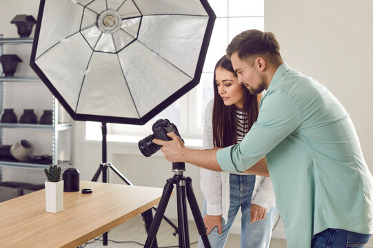 Photographer and model choosing photos from photo shoot together. Side view of portrait of professional photographers couple looking at camera screen in modern studio with professional equipment