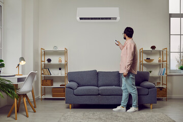 Man uses remote control to turn on or adjust air conditioner hanging in his home office. Man is...