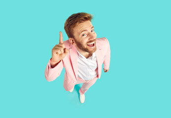 Funny young man in trendy pink suit standing isolated on blue background has good, clever, genius...