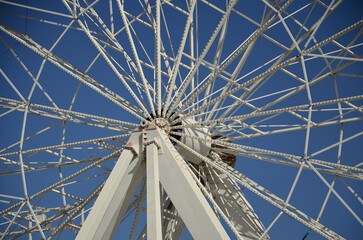 Obraz premium View of the steel structure of a fairground ferris wheel, with the axis, the spokes and the blue sky in the background