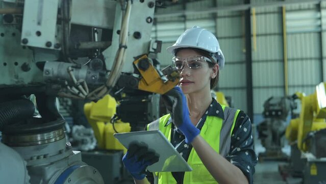 A female engineer installs a program on a robotics arm in a robot warehouse. And test the operation before sending the machine to the customer.