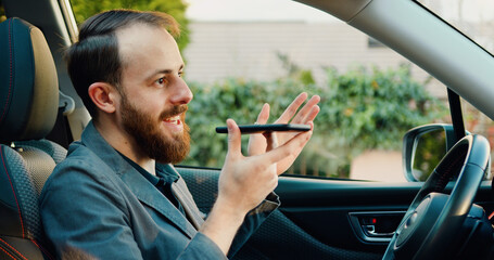 Young man driver recording voice message on phone. Handsome young man in the car is talking voice messages via smartphone.
