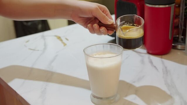 4k video slow motion, pouring brewing espresso shot into glass full of ice. Making black coffee mixed with creamy milk on table. Cold coffee drink glass with ice and milk.