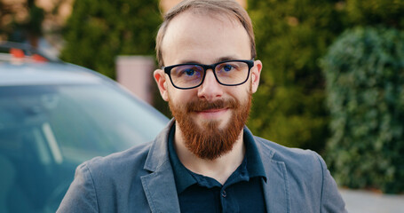 Portrait of businessman in glasses looking at camera standing on city street. Mood change, human emotions and young people concept.