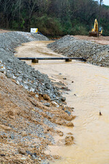 Construction equipment sits unused near a fast flowing stream of muddy water on a construction site.